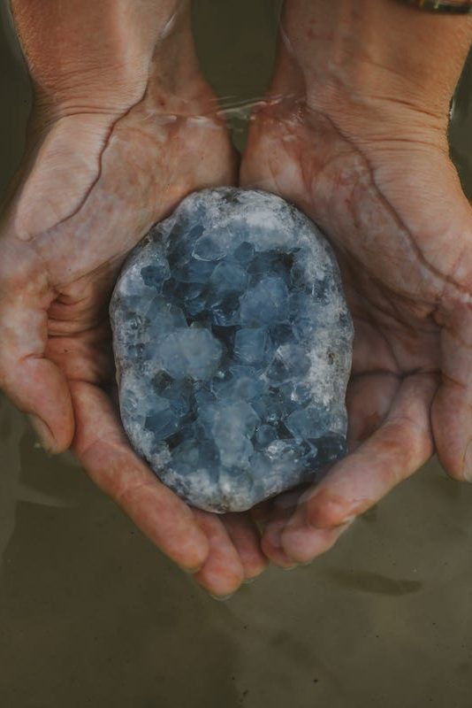 Akashic Record: Hands holding Celestite crystal emerging from the water